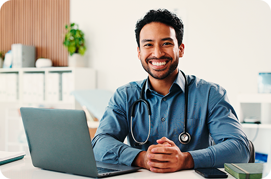 Médico sorri durante teleconsulta em frente ao computador no consultório.
